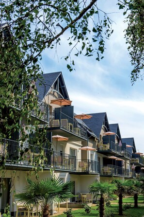 Un hotel de varios pisos con balcones, mobiliario exterior y palmeras.