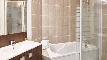A modern bathroom with a large white bathtub, a glass-enclosed shower, and a vanity with a mirror.