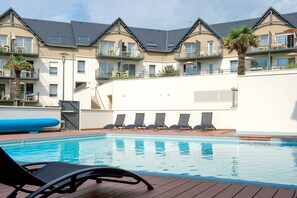 A pool area with lounge chairs, a palm tree, and a building with balconies.