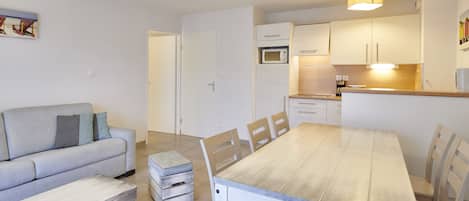 Een moderne keuken met witte kasten, een houten eettafel en een grijze bank.