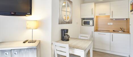 A modern kitchen with white cabinets, a microwave, a coffee maker, and a TV mounted on the wall.
