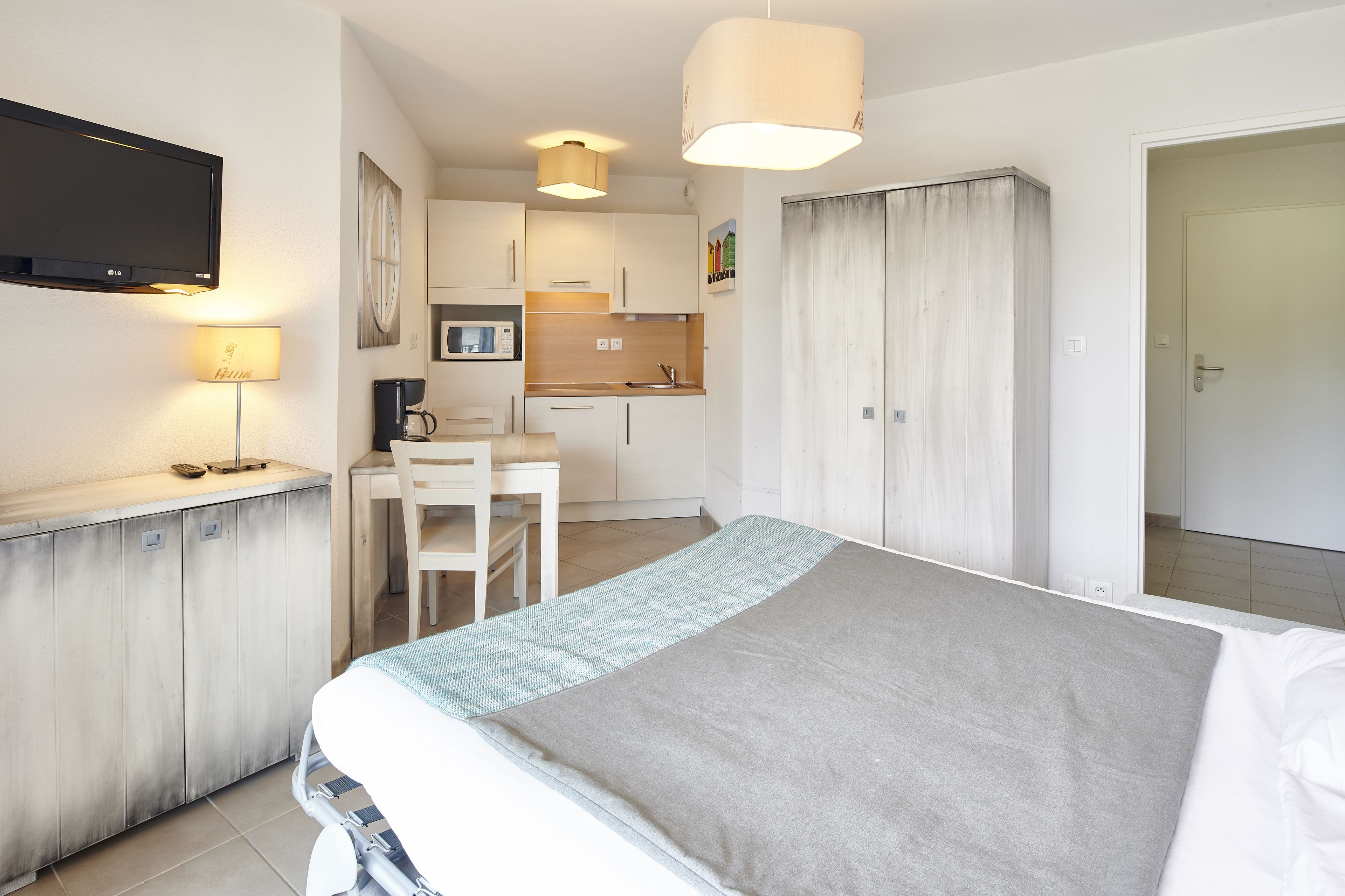 A hotel room with a bed, a desk, a chair, a television, and a kitchenette.