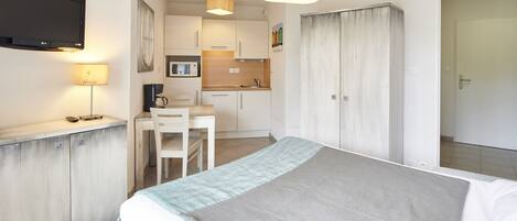 Une chambre d’hôtel équipée d’un lit, d’un bureau, d’une chaise, d’une télévision et d’une kitchenette.