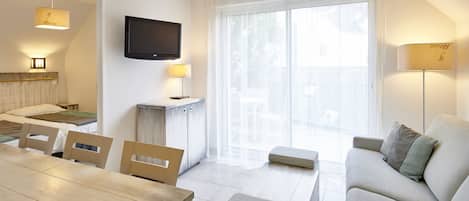 A modern living room with a sofa, a dining table, chairs, a TV, and a large window with curtains.