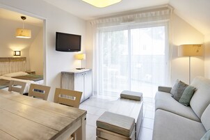 Un salon moderne comprenant un canapé, une table à manger, des chaises, un téléviseur et une grande fenêtre avec des rideaux.