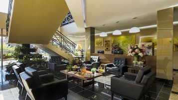 A modern hotel lobby with black leather seating, a wooden coffee table, and a staircase leading to an upper level.