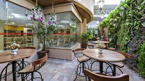 Un patio al aire libre con mesas y sillas de madera redondas, rodeado de plantas y flores exuberantes.