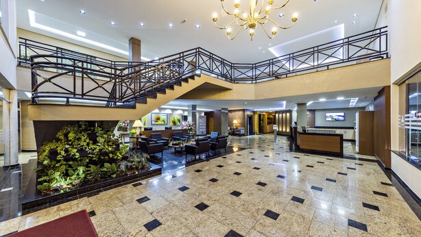 Un vestíbulo amplio con una escalera central, un candelabro y una recepción.