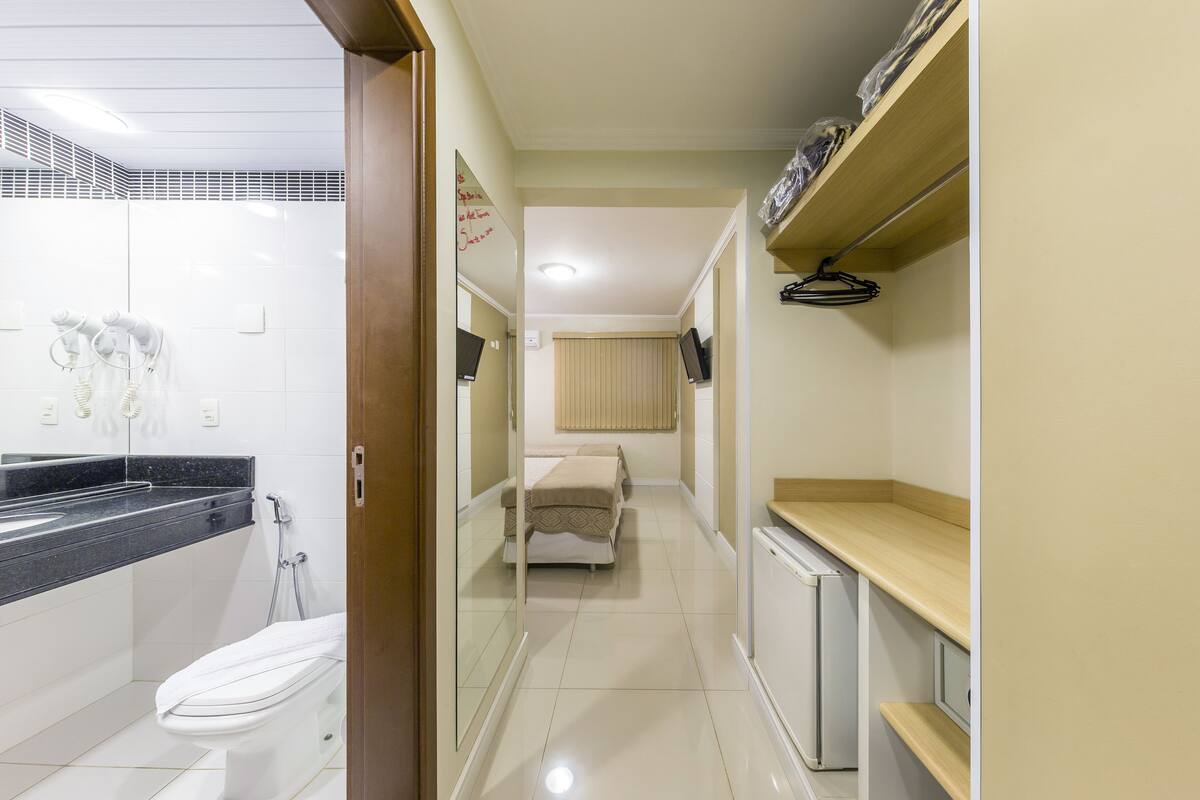 A narrow hallway with a toilet, a bed, and a small kitchenette area.