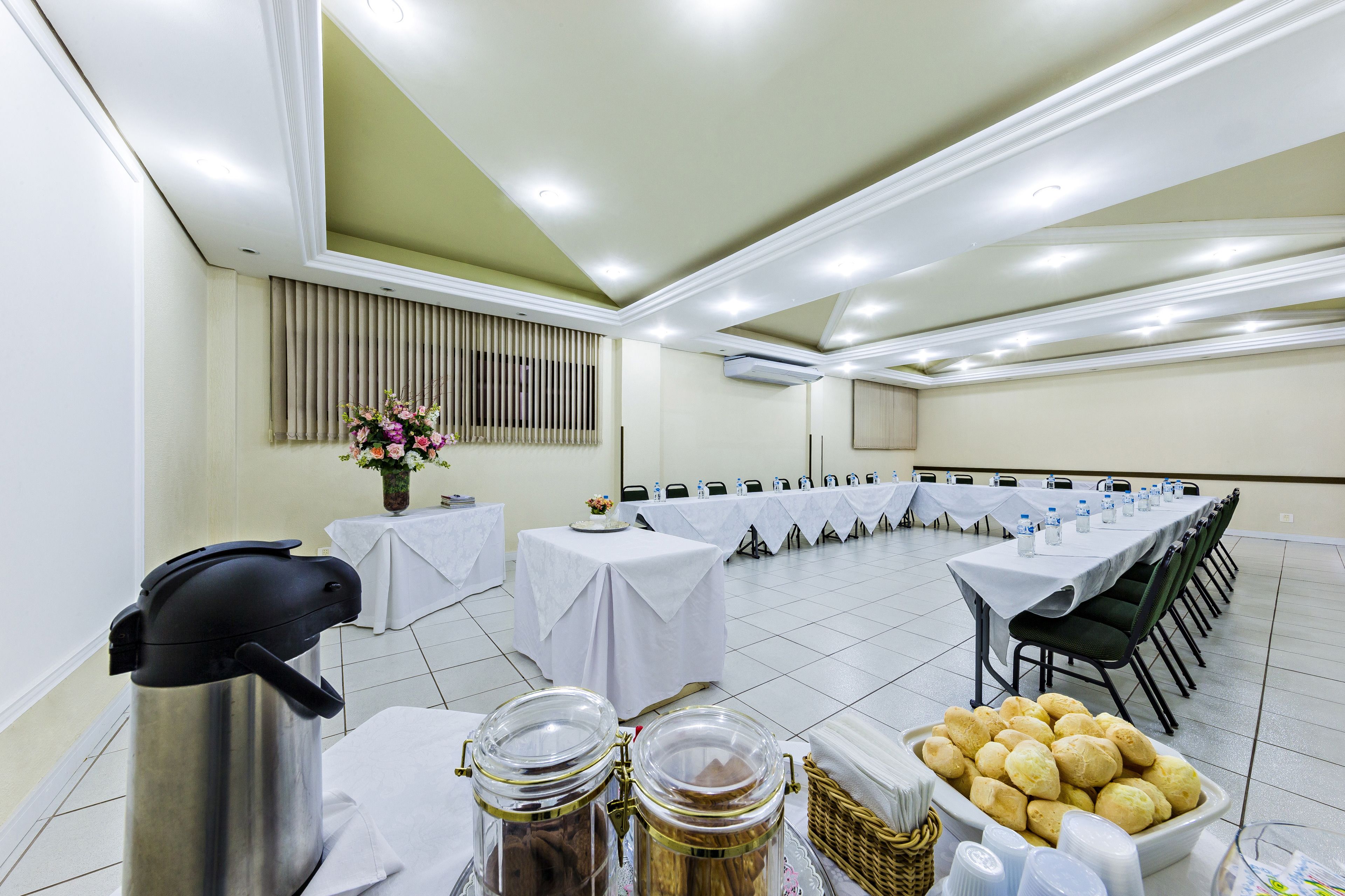 Een vergaderruimte met tafels gedekt voor een vergadering, een koffieapparaat en etenswaren op een tafel.