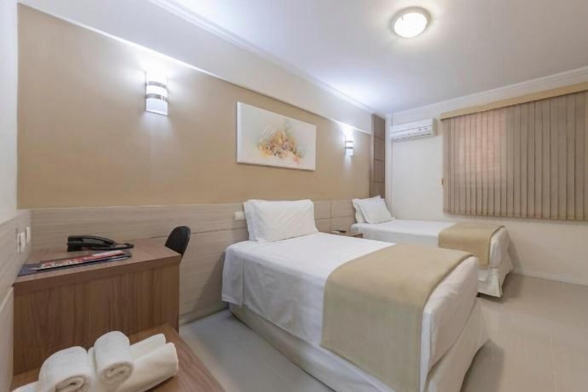 A hotel room with two beds, a desk, a chair, a television, and a window with curtains.