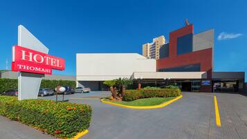 A modern hotel entrance with a prominent sign, landscaped gardens, and a parking area.