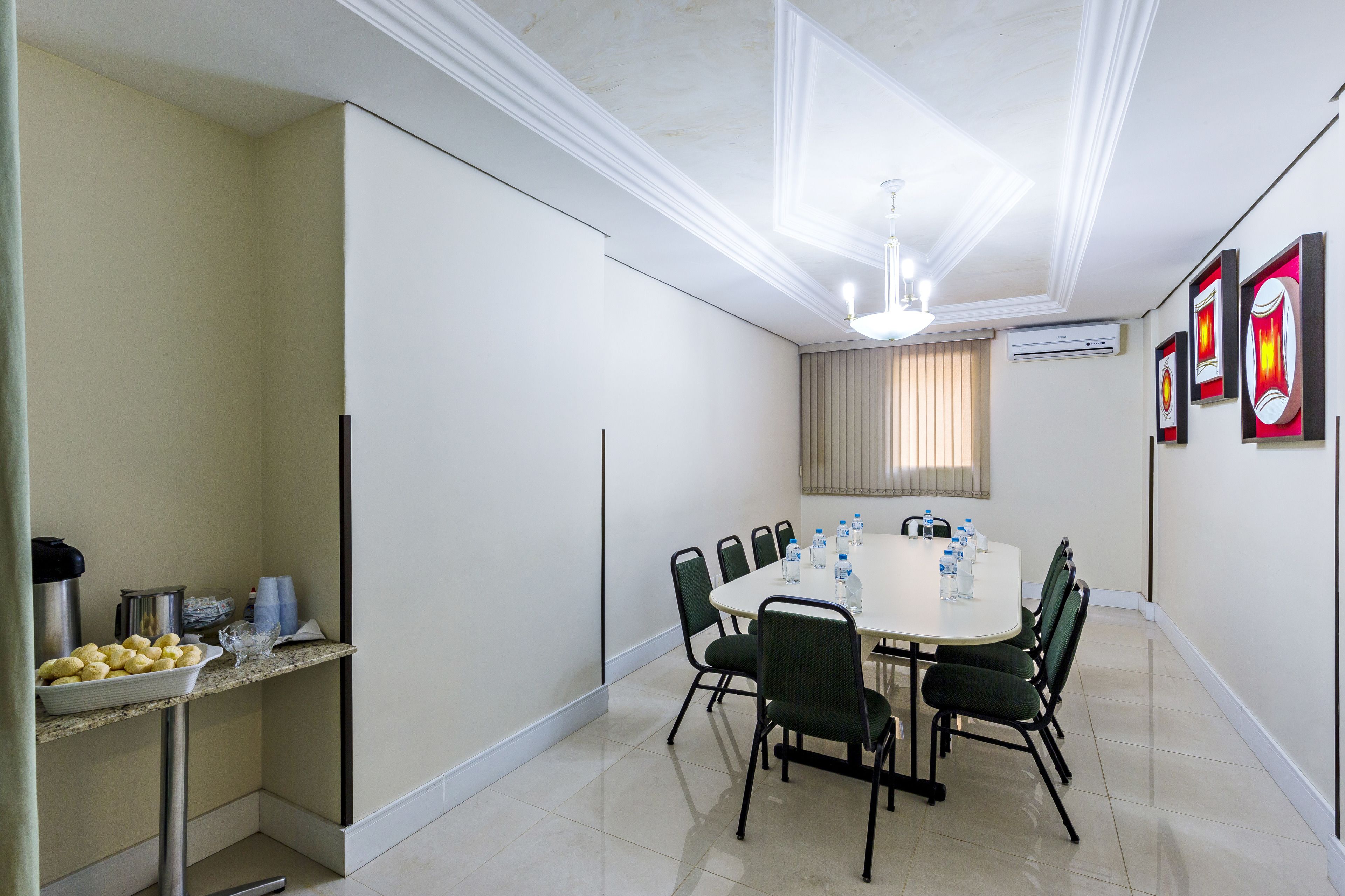A conference room with a round table, chairs, a coffee station, and framed artwork on the walls.