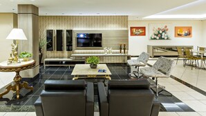 Un moderno hall de hotel con un área de descanso, un televisor, obras de arte en las paredes y una recepción.