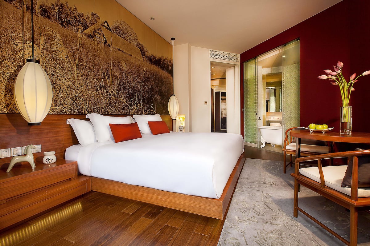 Une chambre d’hôtel moderne dotée d’un grand lit, de tables de chevet en bois, d’un bureau avec des chaises et d’une fresque murale décorative.