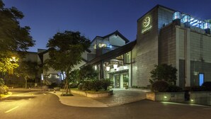 Un edificio moderno con una imponente torre de reloj, una entrada bien iluminada y jardines ajardinados.