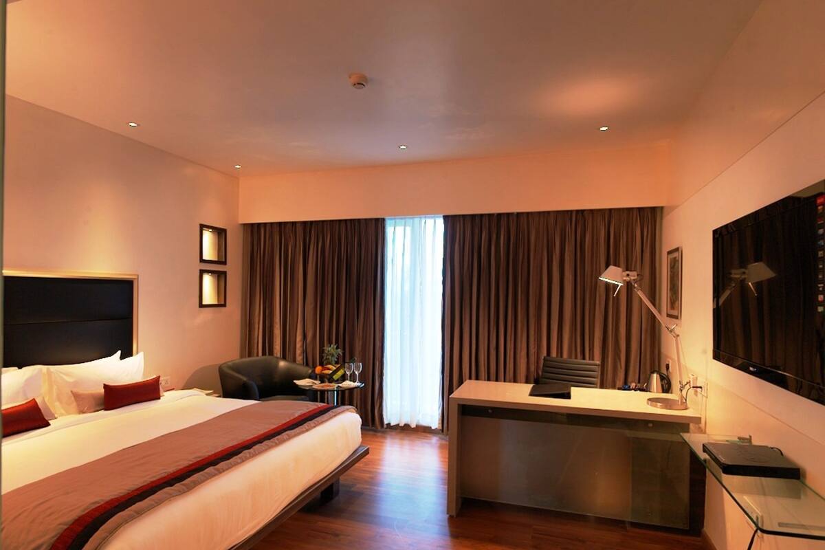 Een hotelkamer met een groot bed, een bureau, een stoel, een bureaulamp, een televisie en een raam met gordijnen.