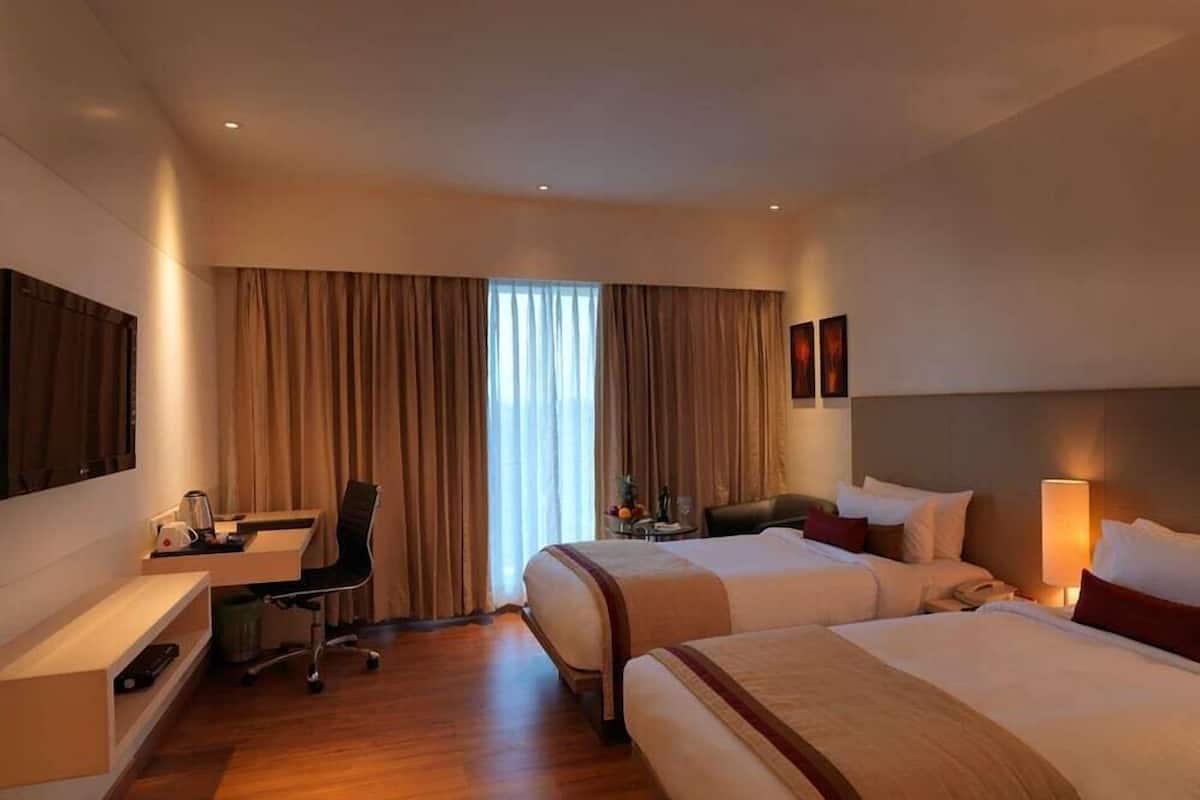 Een hotelkamer met twee bedden, een bureau met stoel, een televisie en een raam met gordijnen.