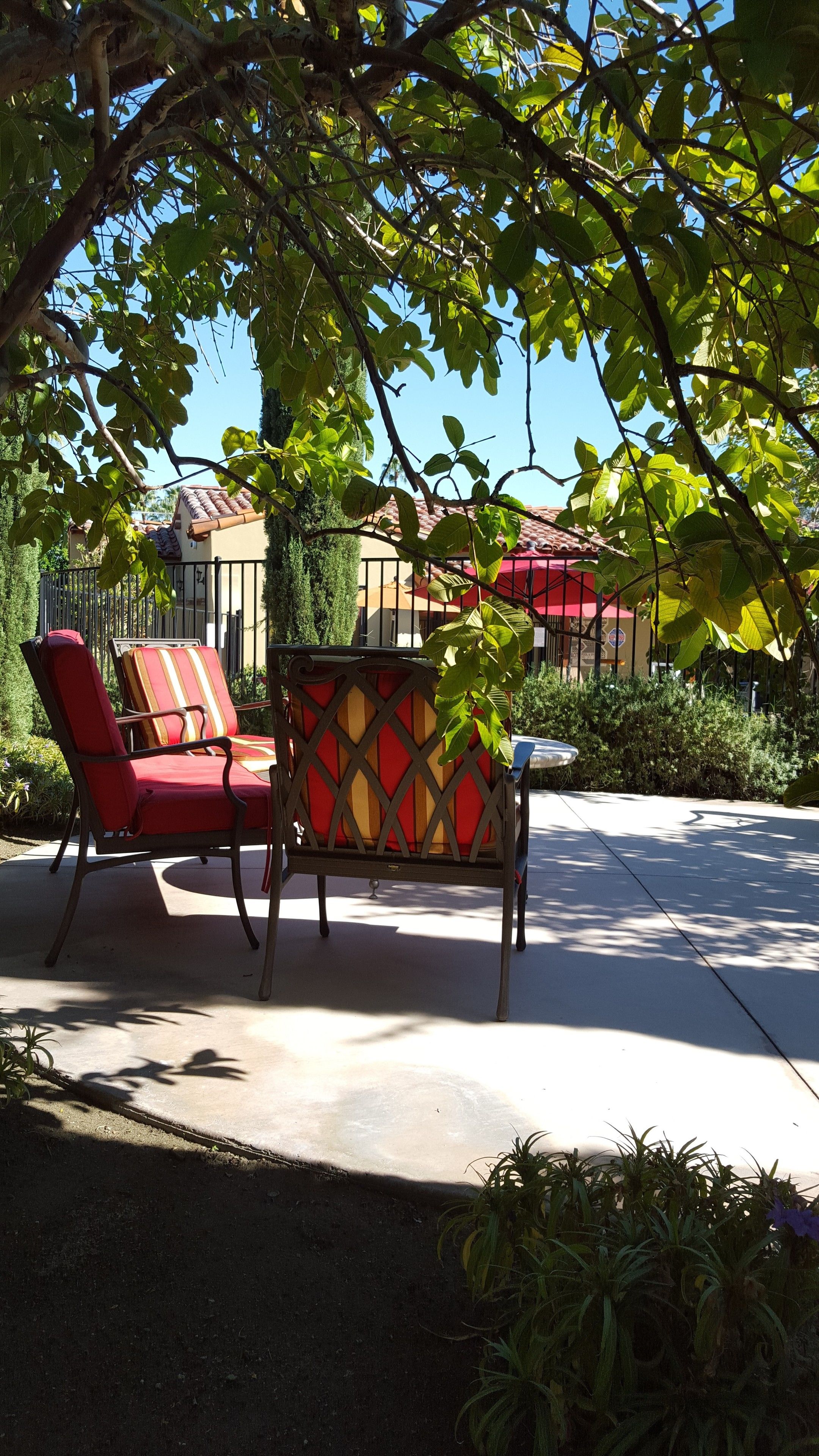 An outdoor seating area with a red and yellow patterned table, two red cushioned chairs, and a small table.