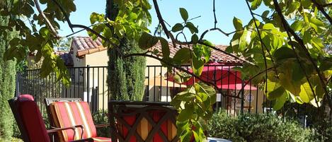 An outdoor seating area with a red and yellow patterned table, two red cushioned chairs, and a small table.