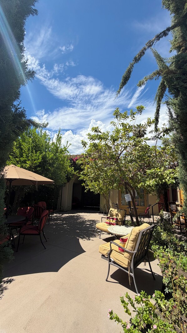An outdoor patio area with a round table and chairs, surrounded by greenery and a clear sky. - Los Arboles Hotel (Palm Springs)