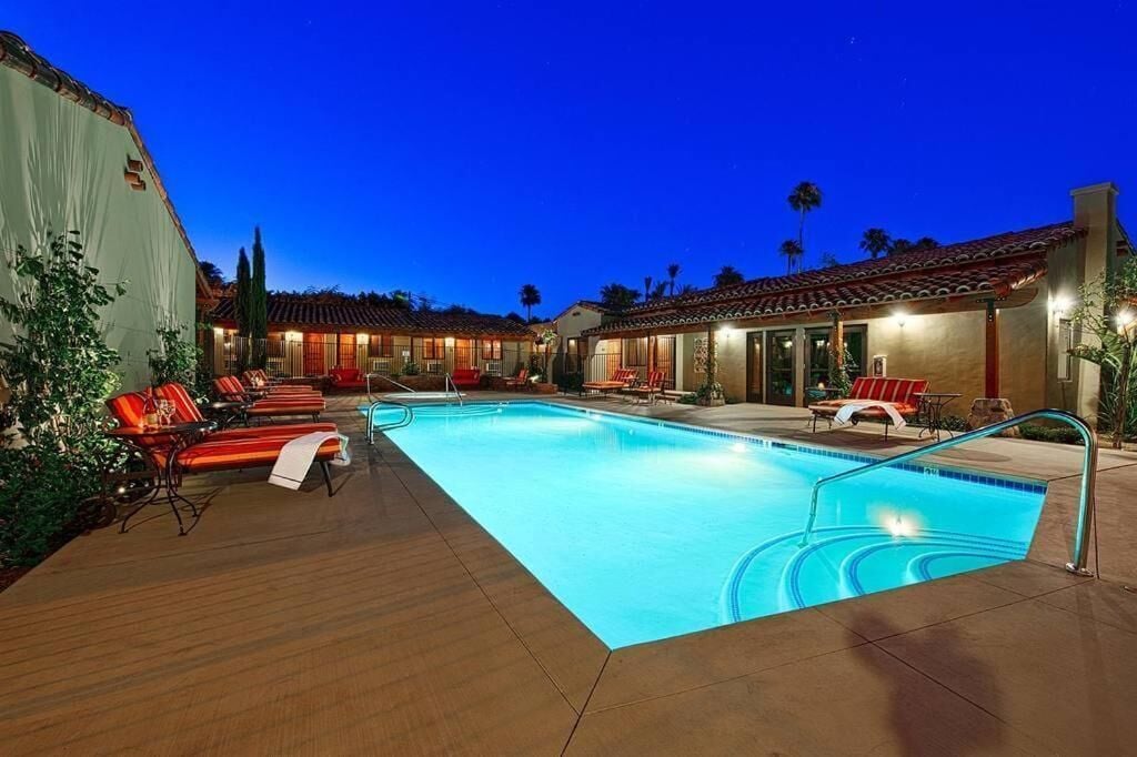 A swimming pool with lounge chairs, a covered patio area, and a building with a tiled roof.