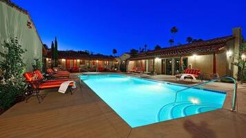 A swimming pool with lounge chairs, a covered patio area, and a building with a tiled roof.