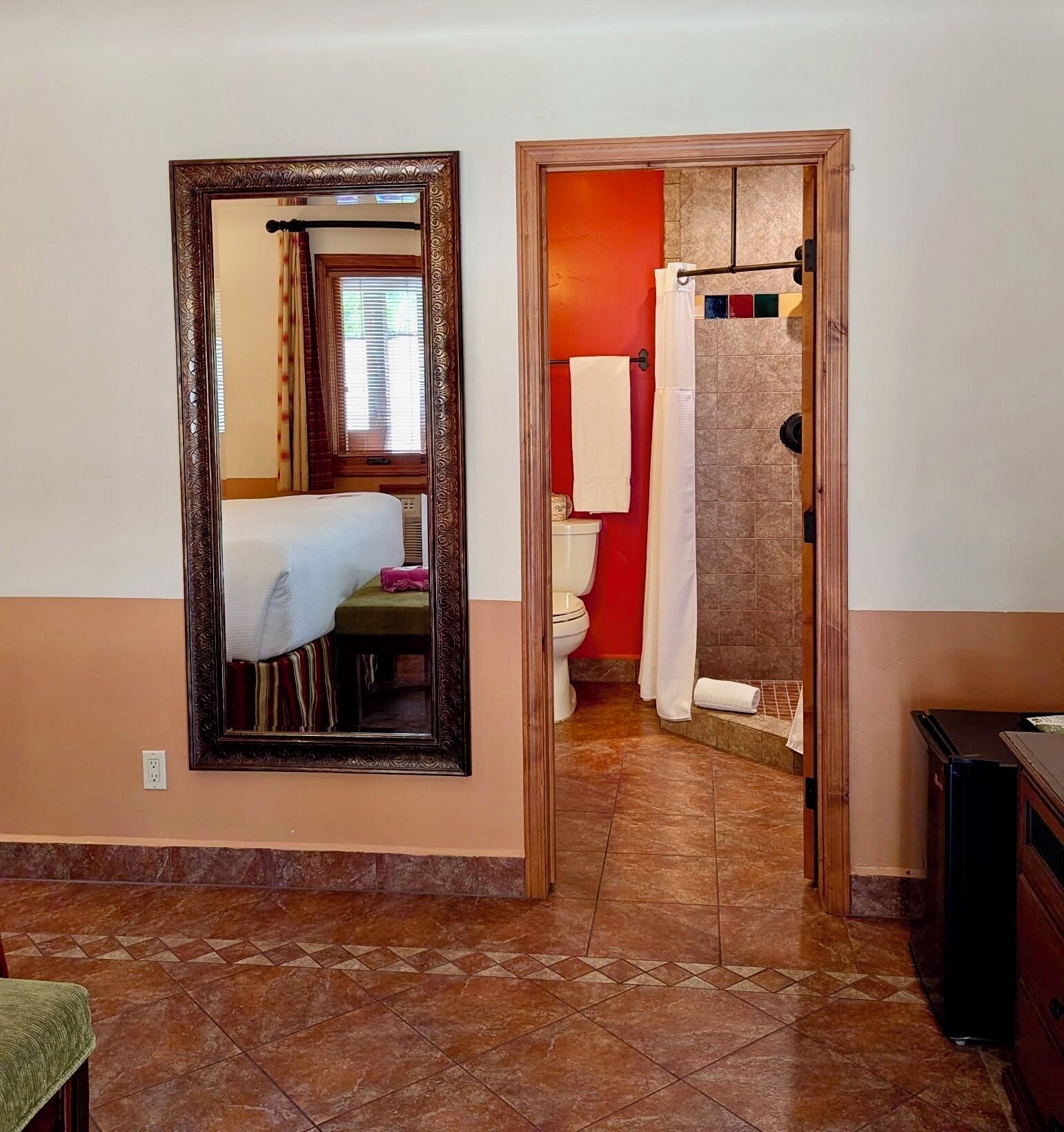 A hallway leading to a bathroom with a toilet, a shower, and a mirror with an ornate frame.