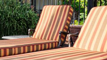 Un conjunto de sillones a rayas con reposabrazos, ubicados al aire libre con una valla metálica y follaje al fondo.