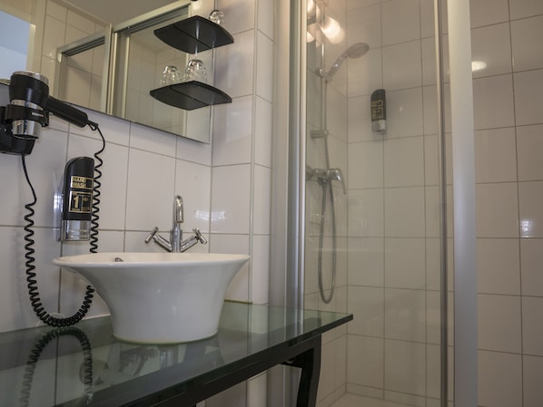 Une salle de bain avec un lavabo blanc, un sèche-cheveux et une cabine de douche en verre.