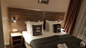 A neatly made bed with pillows, a bedside table, and a headboard. - Hotel Hague Center (The Hague)