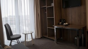 A modern hotel room with a wooden desk, a television mounted on the wall, a chair, and a small table. - Hotel Hague Center (The Hague)
