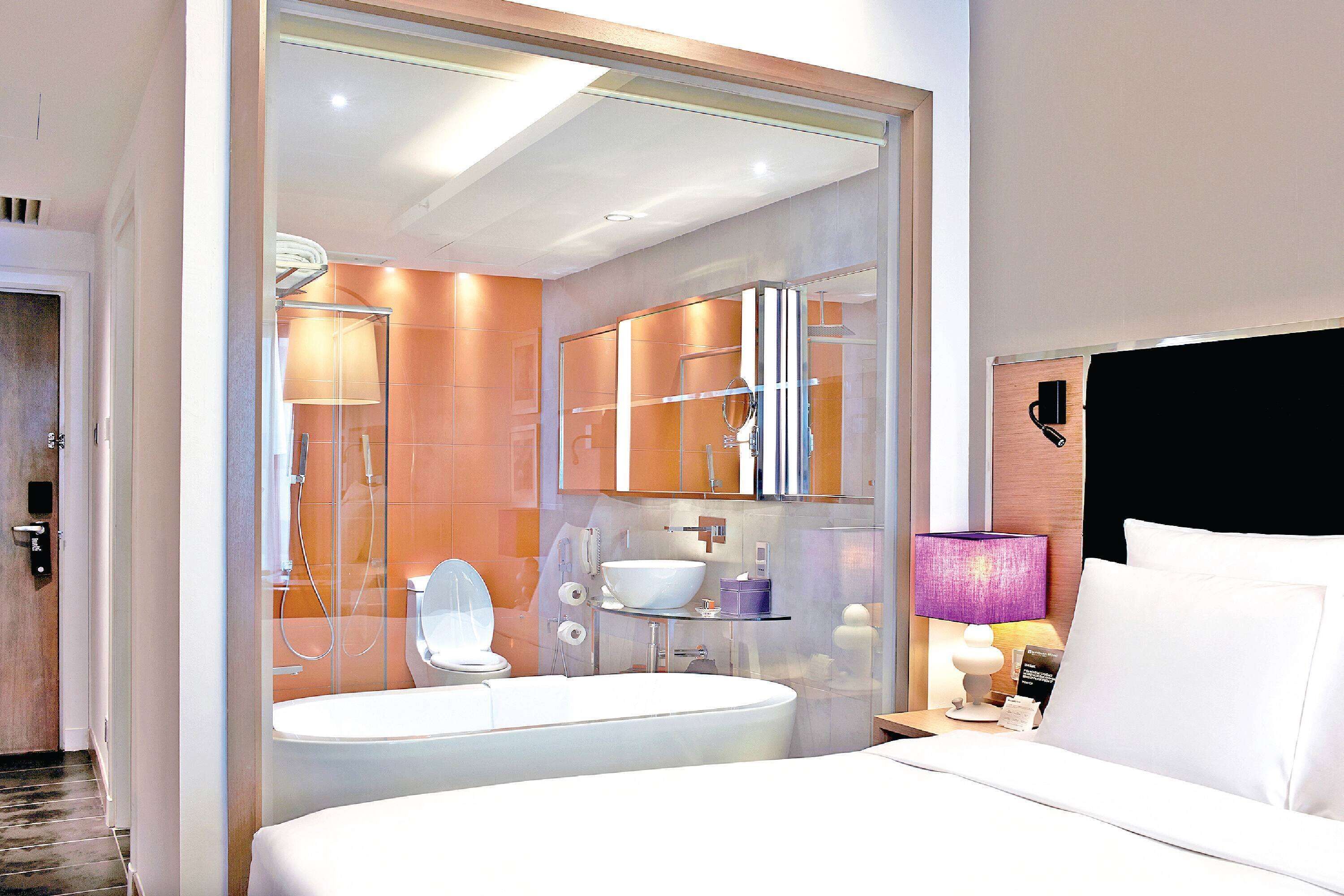 A modern hotel bathroom with a large bathtub, a separate shower area, and a vanity with a mirror.