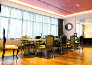 Un comedor con una larga mesa, varias sillas y un amplio ventanal con cortinas.