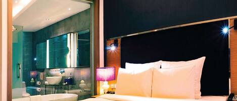 A hotel room with a bed, a nightstand with a phone, a lamp, and a view of the bathroom.