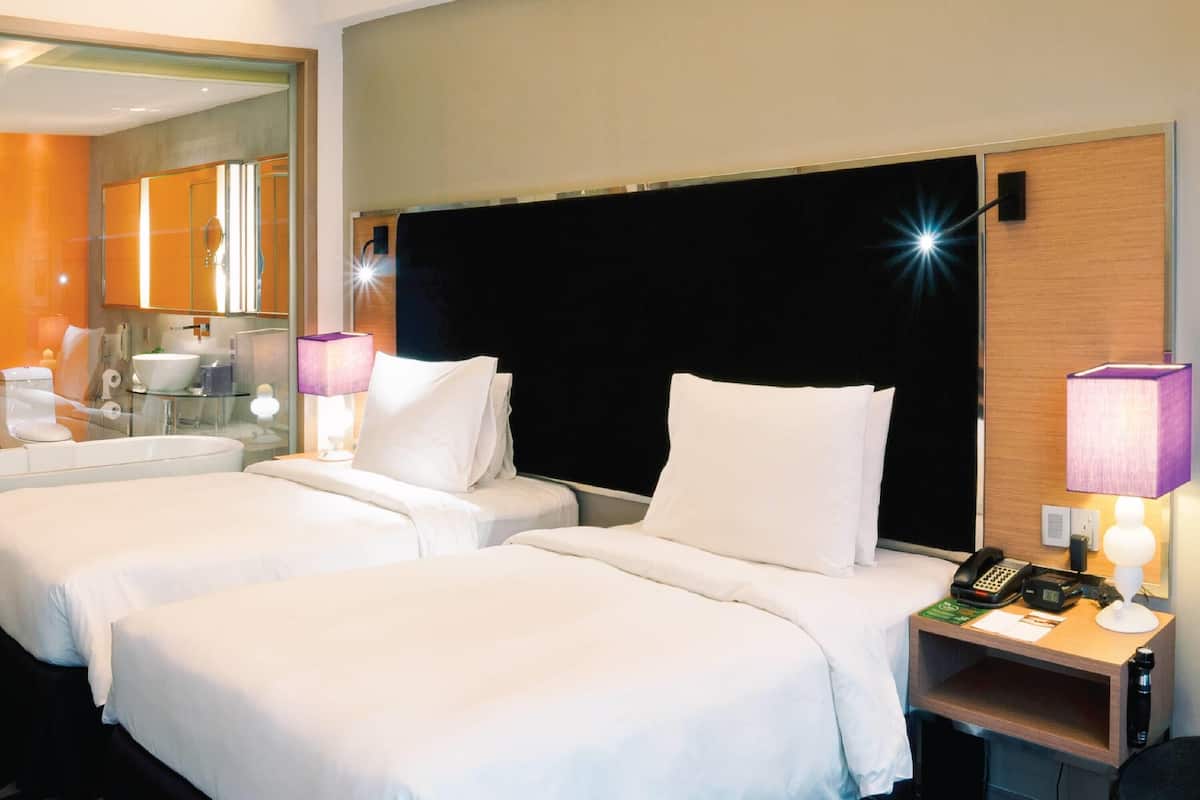 A hotel room with two beds, a bathroom, and a nightstand with a lamp and phone.