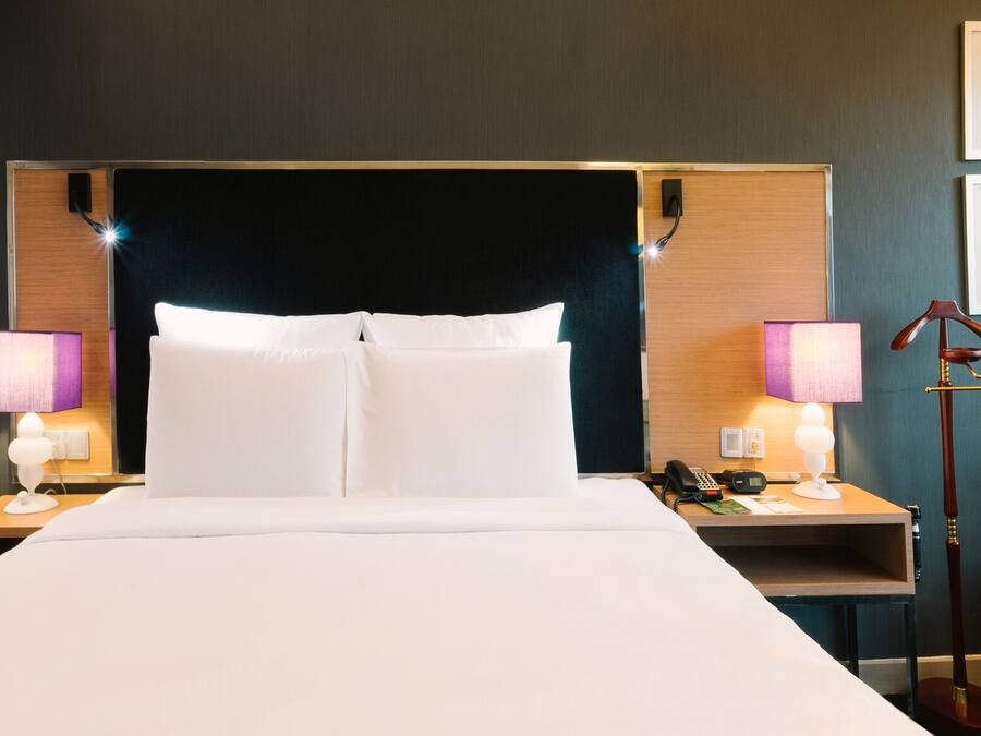 Une chambre d’hôtel avec un grand lit, des tables de chevet avec des lampes, un bureau, une chaise et des tableaux encadrés au mur.
