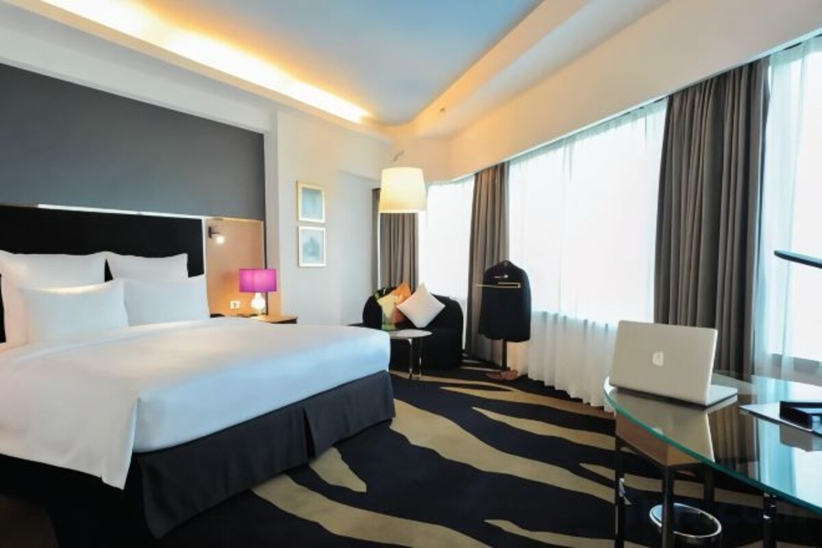 A hotel room with a large bed, a desk with a laptop, a chair, a lamp, and a view of the outdoors.