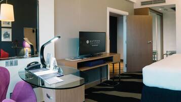 A hotel room with a bed, a desk with a computer, a television, and a bathroom door.