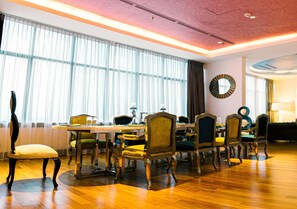 Un coin repas avec une table et des chaises en bois, de grandes fenêtres ornées de rideaux légers et un grand miroir rond accroché au mur.