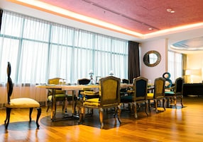 A dining area with a wooden table and chairs, large windows with sheer curtains, and a round mirror on the wall.