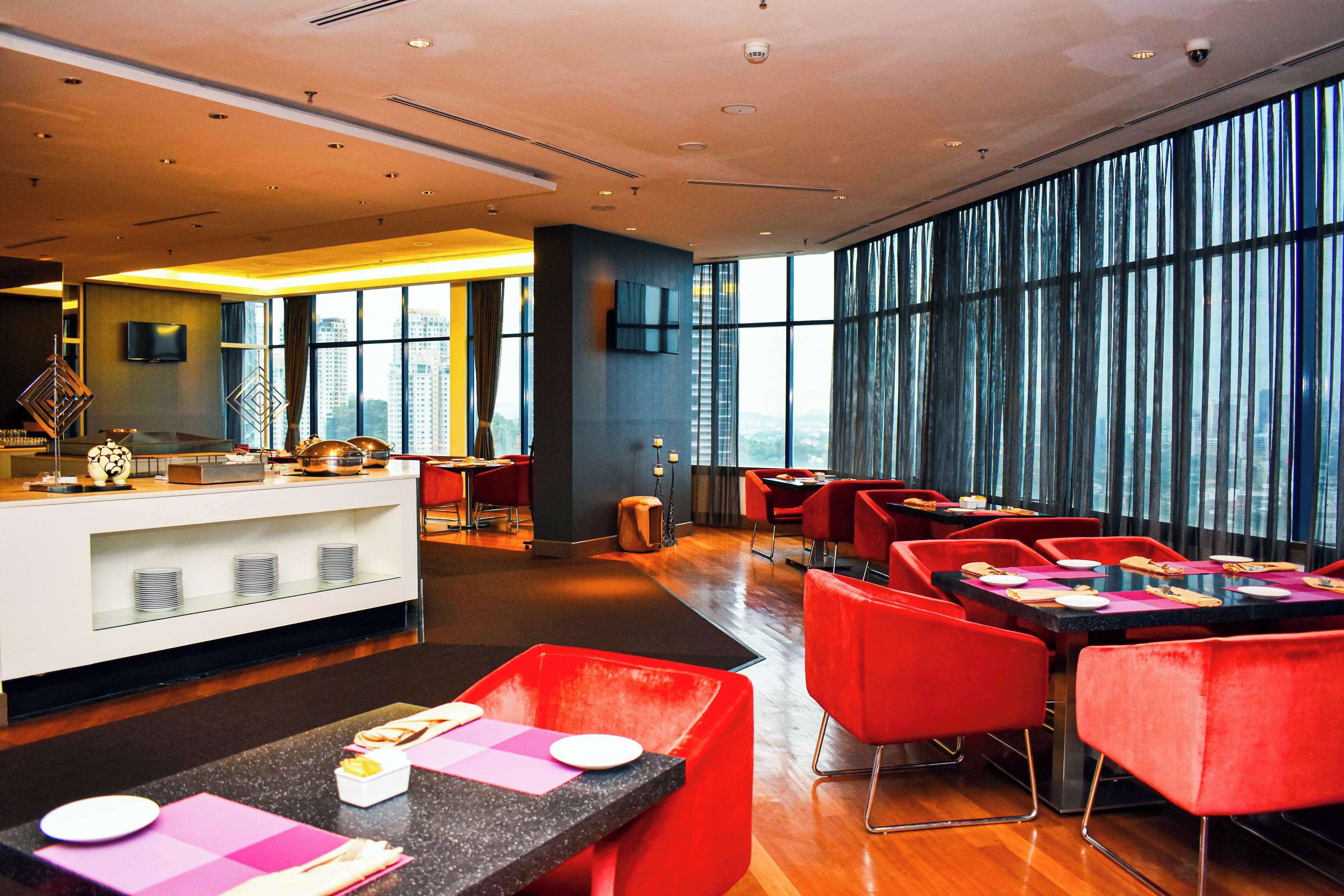 A modern restaurant with a bar area, red seating, and large windows offering a city view.