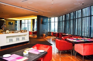 Un restaurante moderno con barra, asientos rojos y grandes ventanales con vistas a la ciudad.