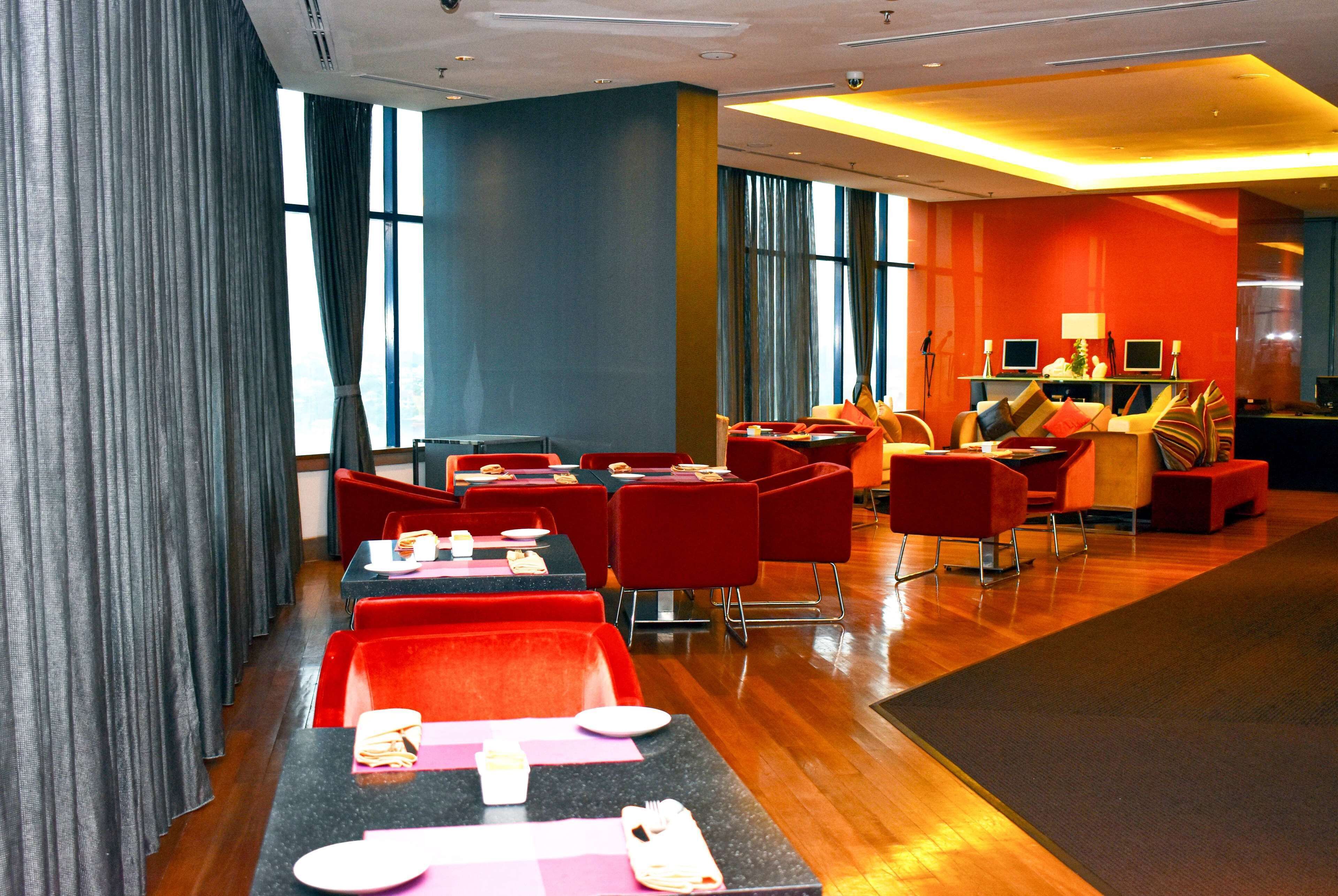 Un moderno vestíbulo de hotel con zona de comedor, mobiliario rojo y amplios ventanales.