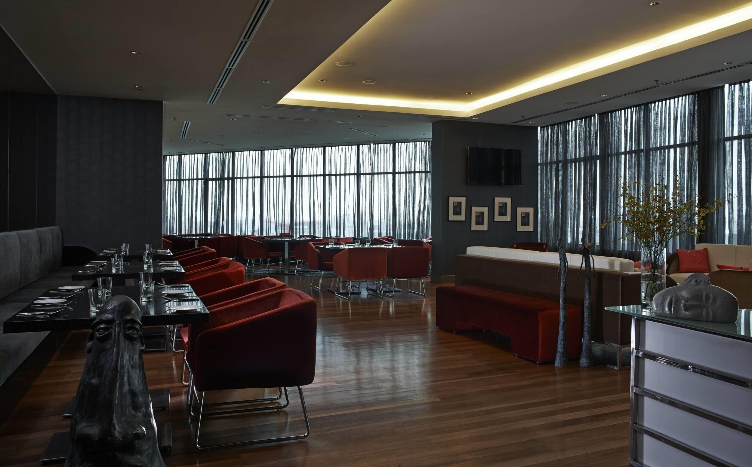 A modern dining area with wooden flooring, red upholstered chairs, and a long table set for dining.