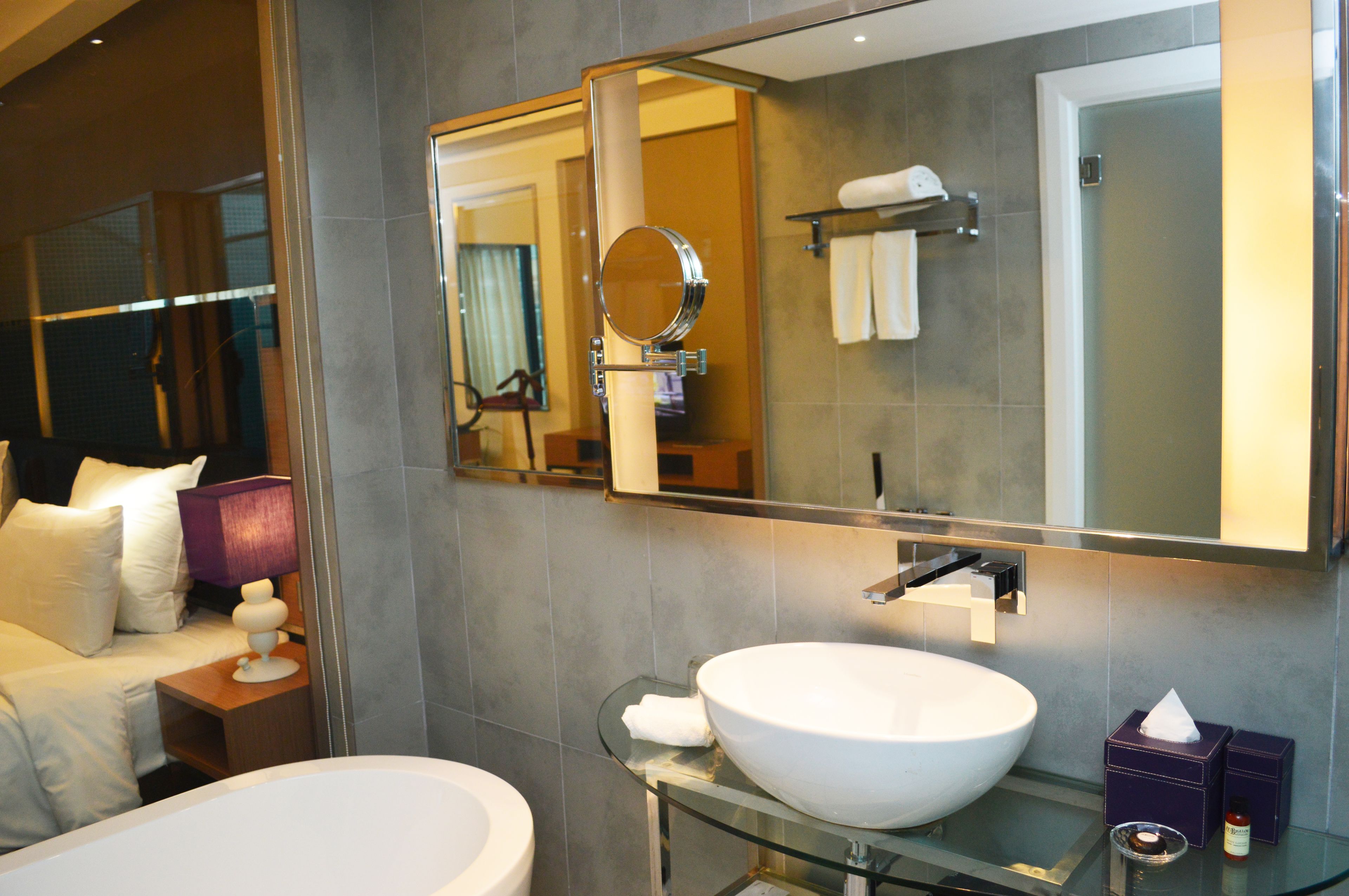 A modern bathroom with a large mirror, a glass-enclosed sink, and a toilet.