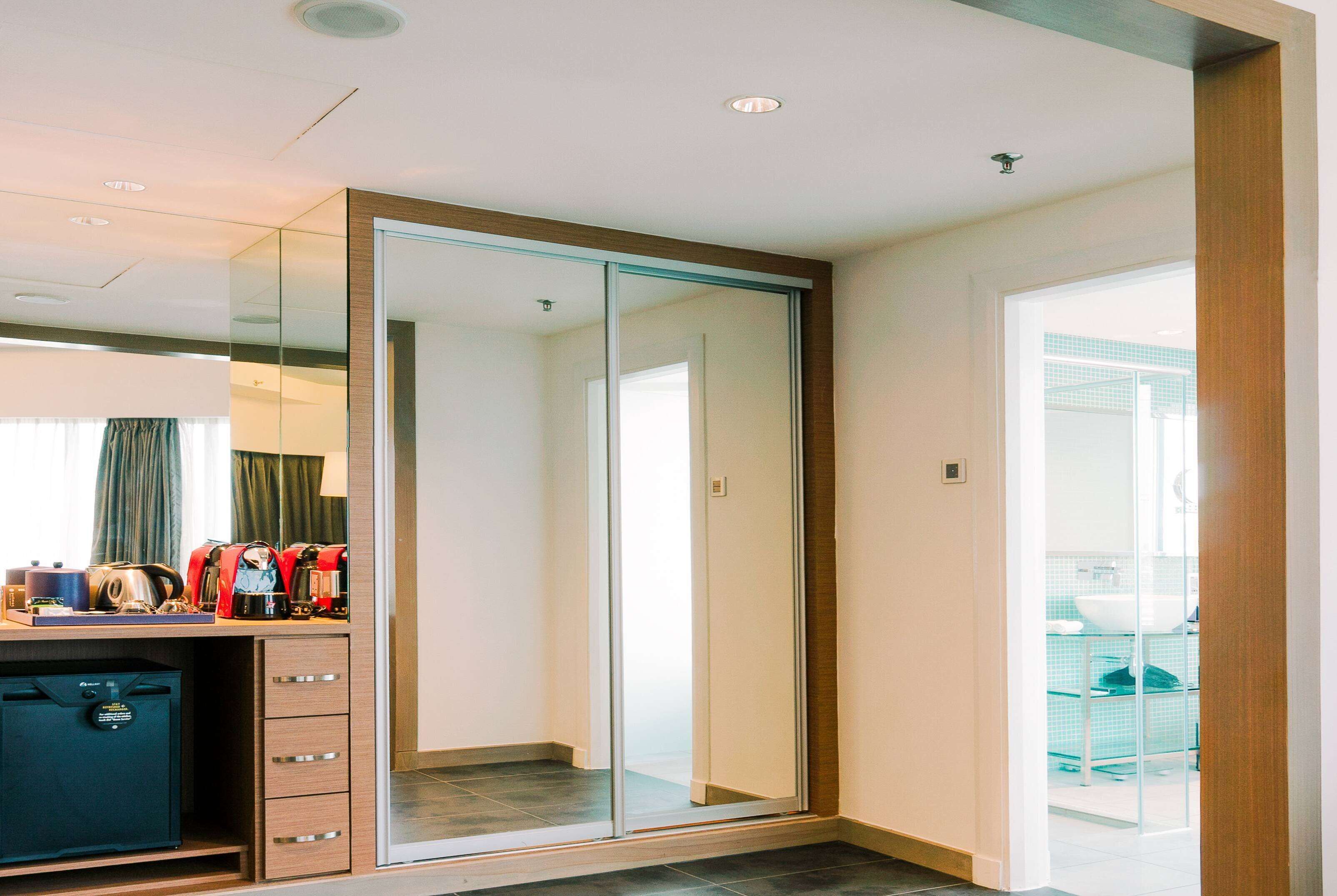 A hotel room with a wardrobe, a desk with a coffee maker, and a view of the outside.