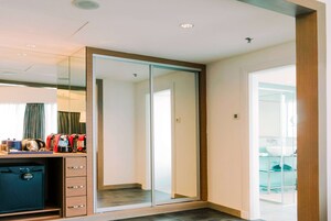 A hotel room with a wardrobe, a desk with a coffee maker, and a view of the outside.