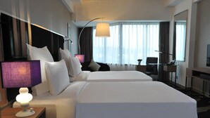 A hotel room with two beds, a desk, a chair, a lamp, and a large window with curtains. - Wyndham Grand Bangsar Kuala Lumpur (Kuala Lumpur)