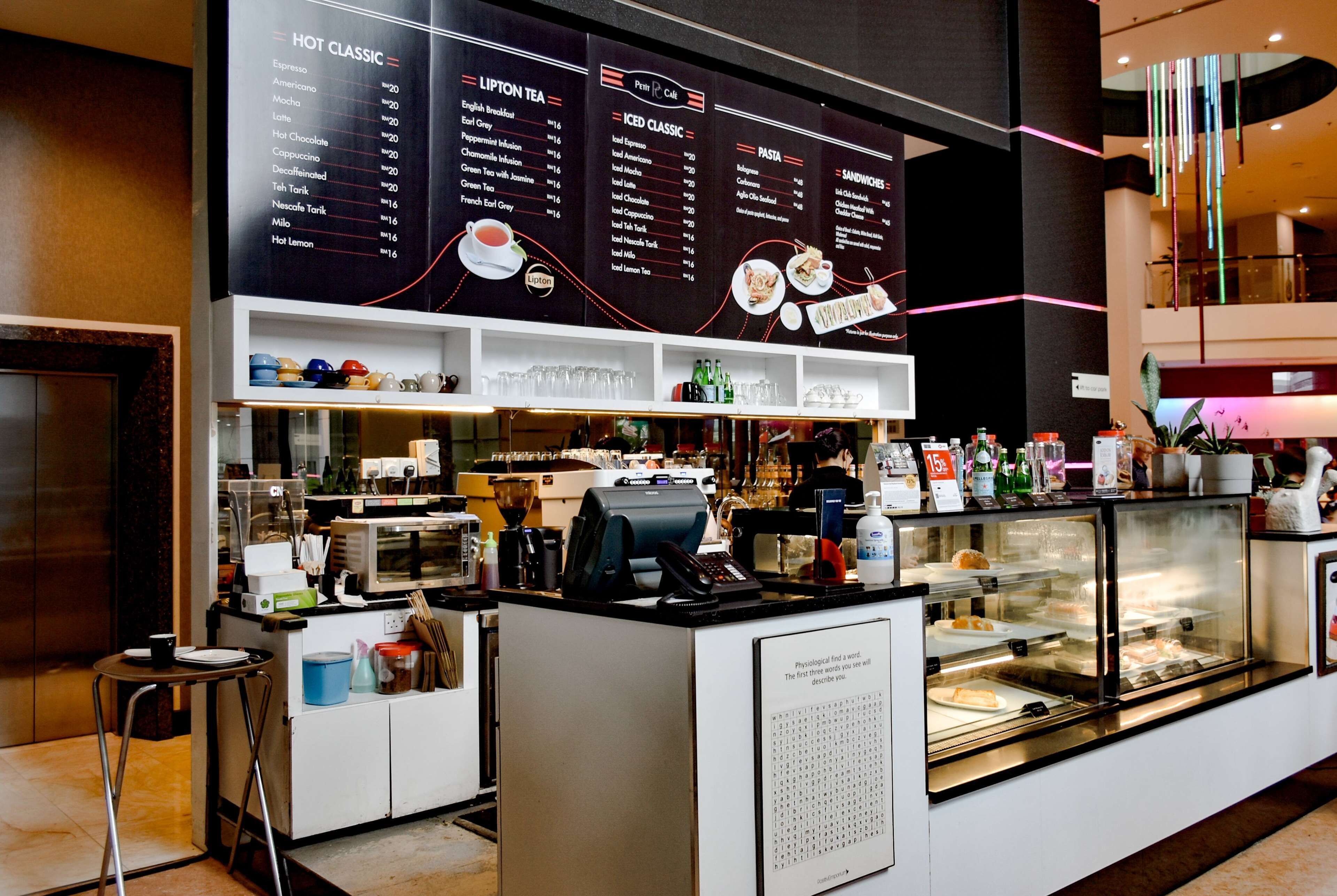 Una cafetería con un menú en la pizarra, máquinas de espresso y una vitrina con pasteles.
